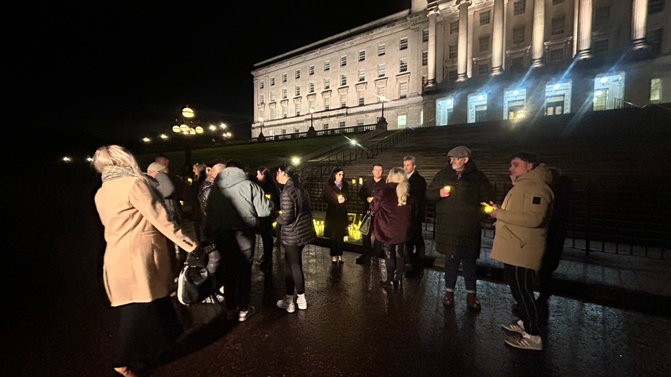 Group of people holding candles with Stormont parliament buildings in the background