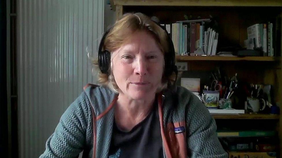 Rebecca Allen, with short brown hair, sitting at a desk with a headset on