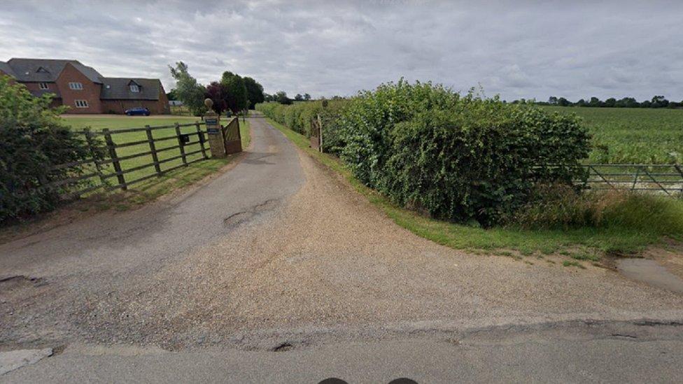 Entrance into a farm. Hedge to the right and fence to the left. Name plaques say "Ferndown" and "Pastures Farm"