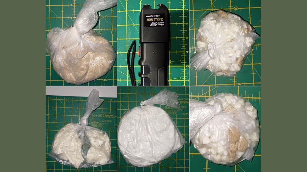 Five plastic bags of white and brown powders and a stun gun all displayed on a green table. 