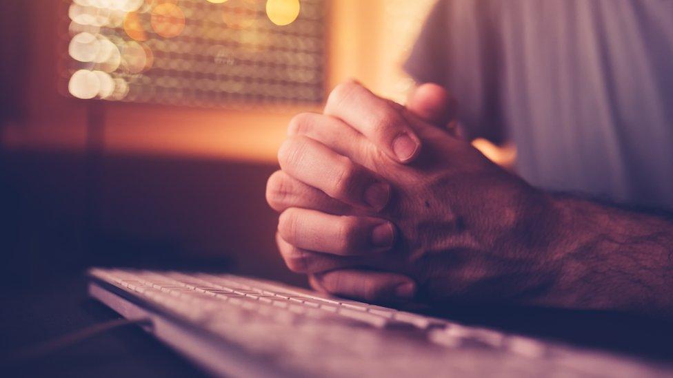 Man with hands clasped at keyboard