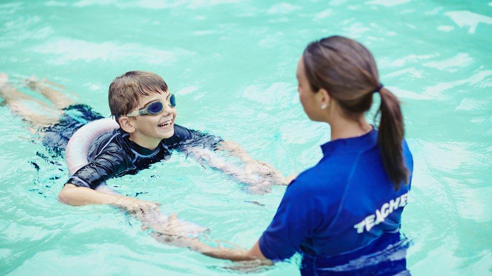 Young boy learning to swim in pool with teacher - stock photo