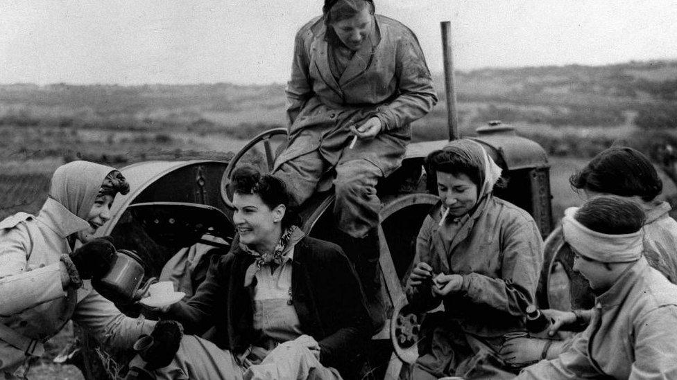 Women sitting on and around a tractor, smoking cigarettes