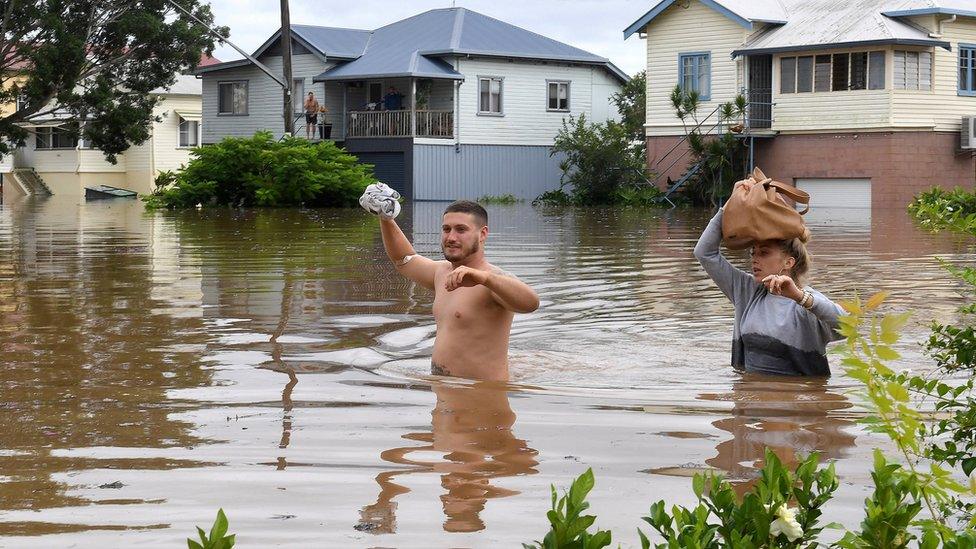 Two people wade through waist-deep water in Lismore.