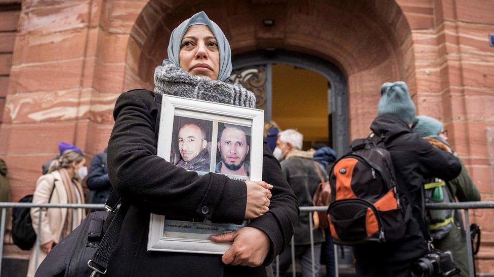 Syrian campaigner of the Caesar Families Association Yasmen Almashan holds pictures of victims of the Syrian regime as she and others wait outside the courthouse where former Syrian intelligence officer Anwar Raslan is on trial in Koblenz, western Germany on January 13, 2022