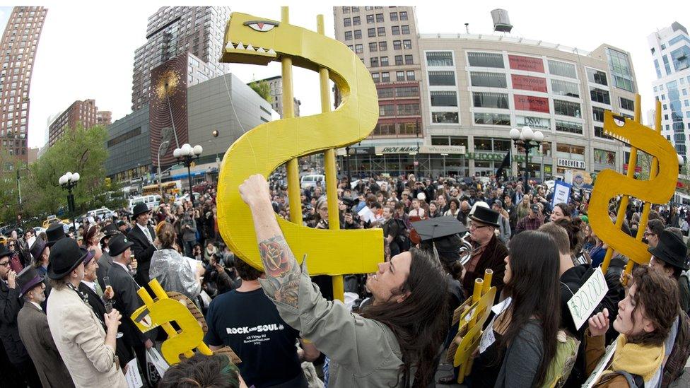 A young man holds up a dollar sign during an Occupy Wall Street rally against the high cost of college tuitions April 25, 2012 in New York. Scores of students and former students gathered to complain about the high cost of tuitions and college loans. April 25th marked the day when US student debt reached USD 1 trillion