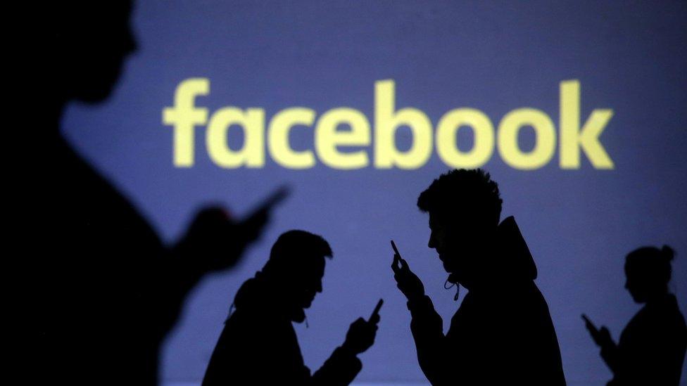 Silhouettes of mobile users are seen next to a screen projection of Facebook logo in this picture illustration taken March 28, 2018.