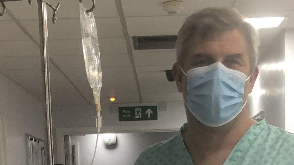 Mr Cock in a face mask next to a drip in hospital