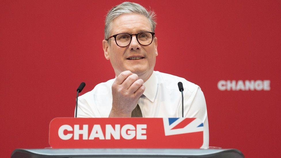 Sir Keir Starmer smiling in front of a podium with the word "change" written on it 