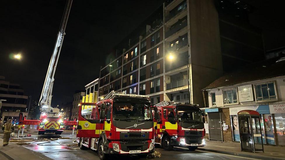 Fire engines in the street in front of a block of flats at night.