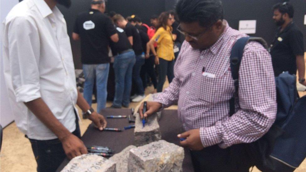 Man signs his name on a stone brick