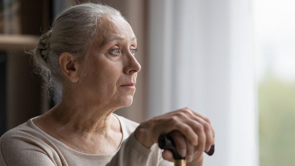 older woman sitting with her hands on a cane