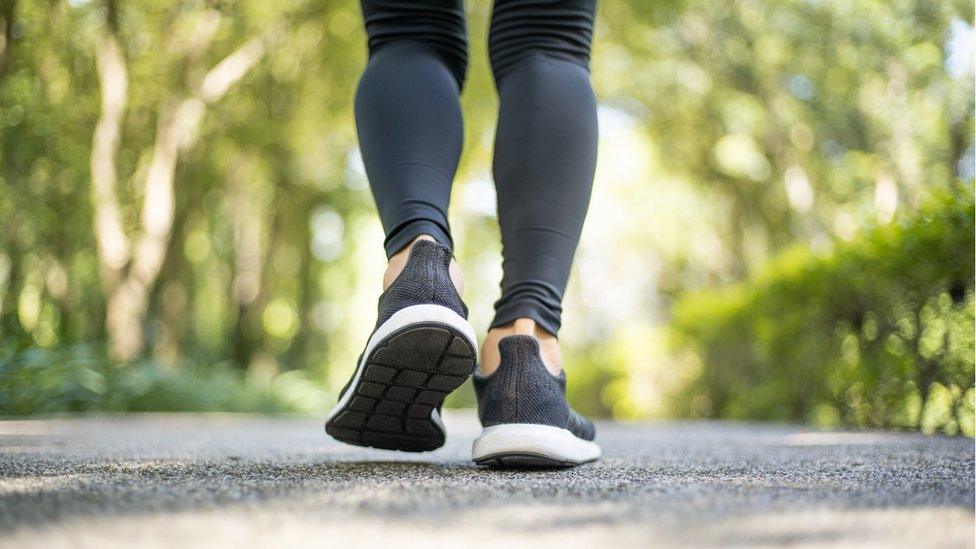 A woman in black leggings walks down a country path