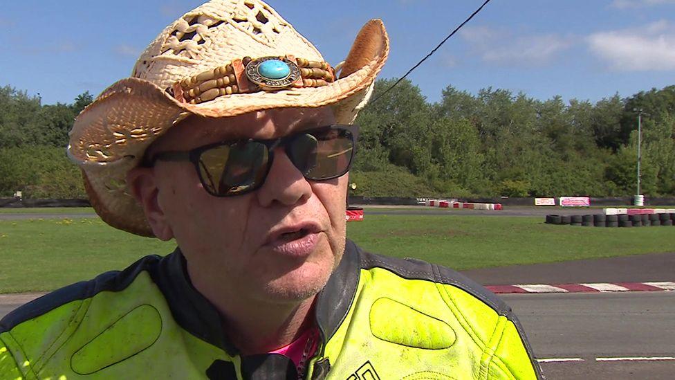 Nigel Limbs wearing a straw hat and sunglasses and his yellow racing leathers