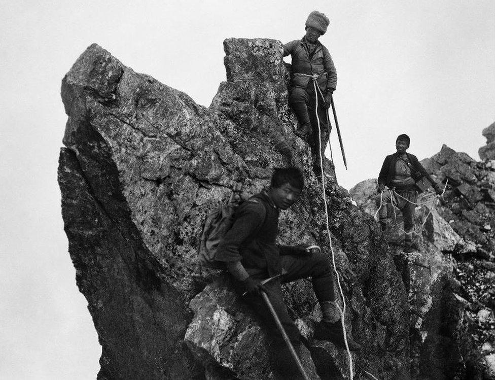 Three porters climbing along a ridge