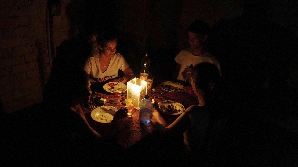 A Cuban family sit in the dark around a candle eating food due to power outage.