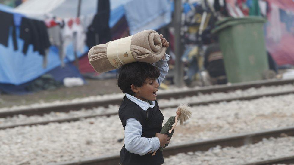 A child plays with a doll while carrying a blanket at the Idomeni camp in Greece.