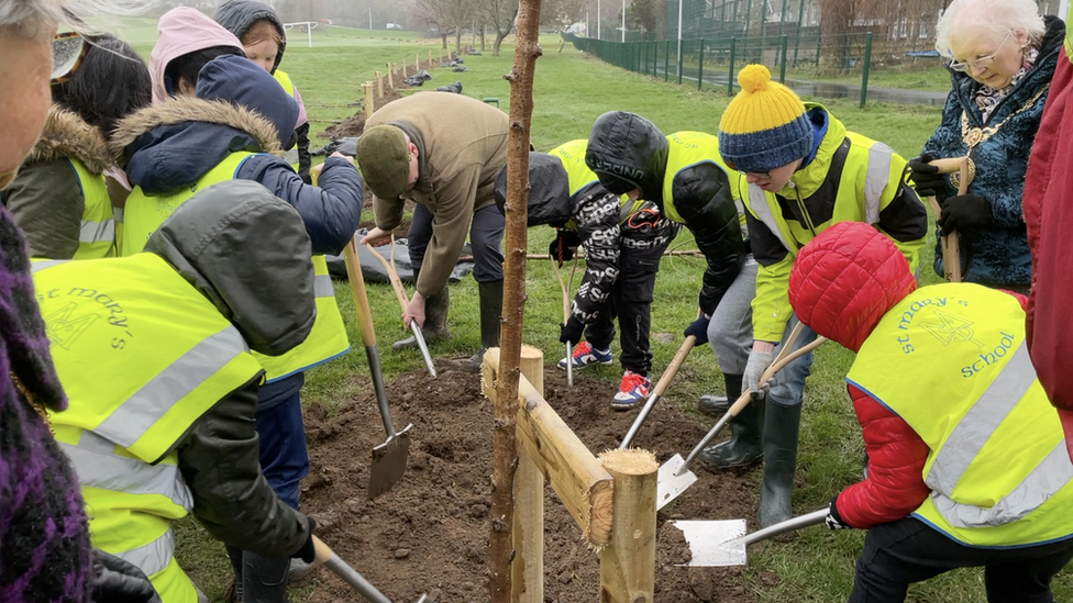 Schoolchildren alongside the lieutenant governor planting the first tree