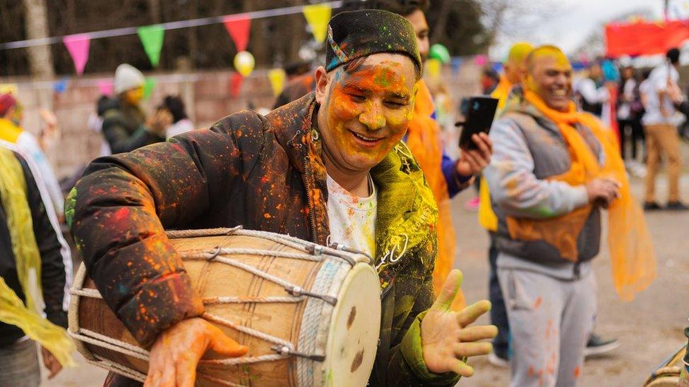 A man playing a dhol drum at a Holi celebration