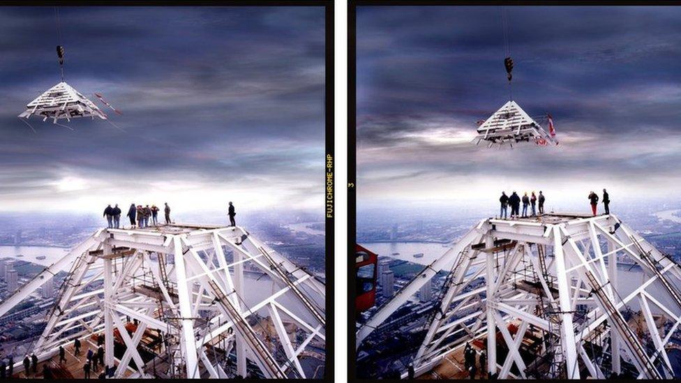 Seven steel workers look up into the air as the pyramid topper is lifted into place by the crane.