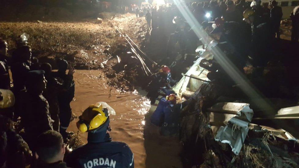 Rescue workers in Jordan wade through debris in a flooded area overnight