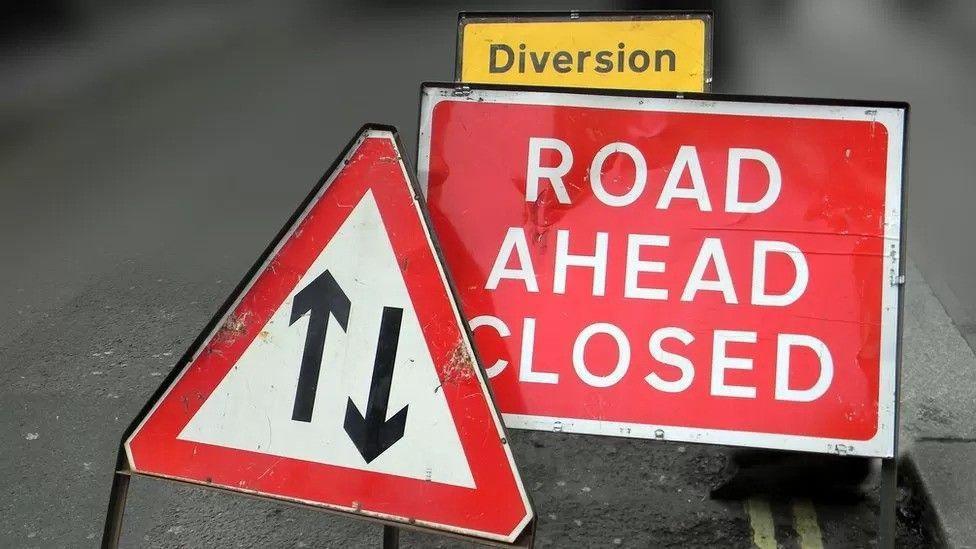 A number of road closure signs on the side of a road. 