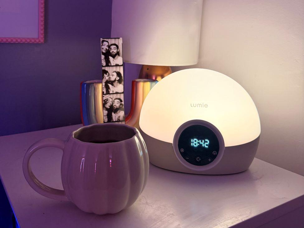 An alarm clock, a mug, a lamp and a photobooth strip laid out on a bedside table