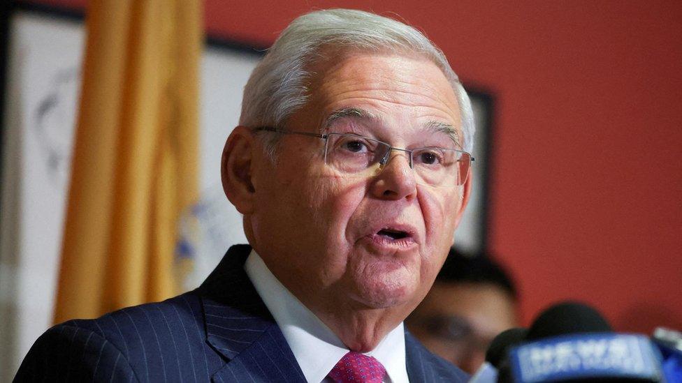 Bob Menendez before yellow flag and red wall speaks to microphone.