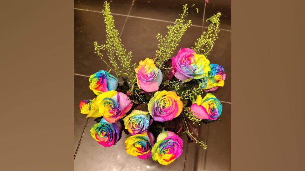 A bunch of vividly coloured roses in shades of pink, blue, violet, green, yellow