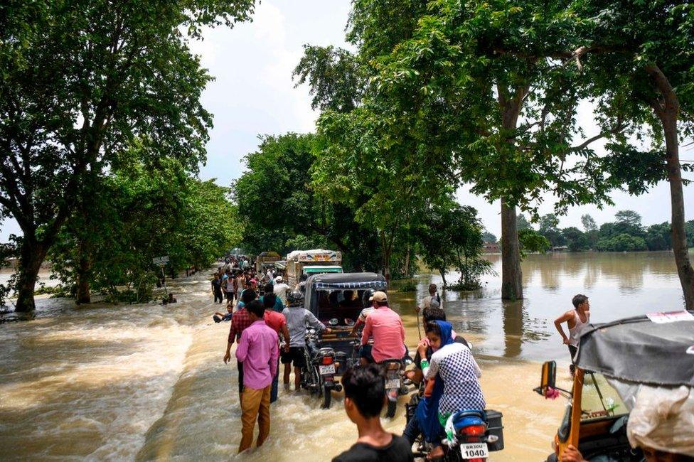 Indian residents drive their vehicles along a flooded road following heavy monsoon rains at Sitamarhi district in the Indian state of Bihar.