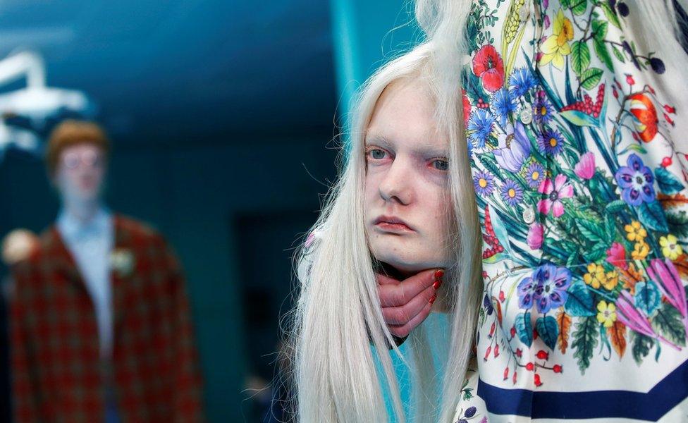 Close-up of female model in floral dress holding a mannequin head that is a replica of her head