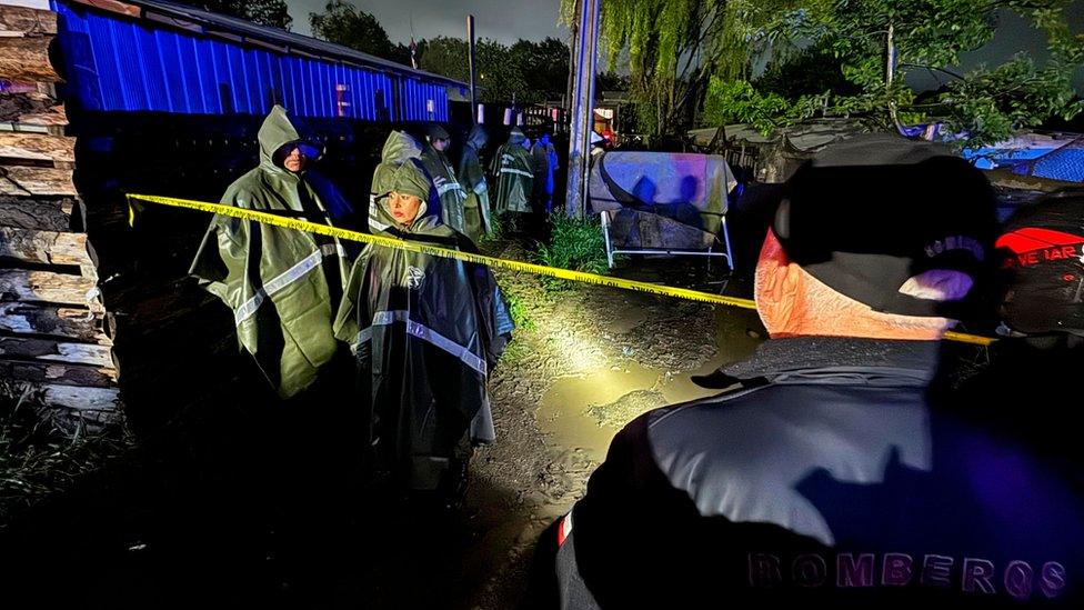 Firegighters and police members inspect the area after a fire tore through a housing settlement killing 14 Venezuelan migrants, including eight children