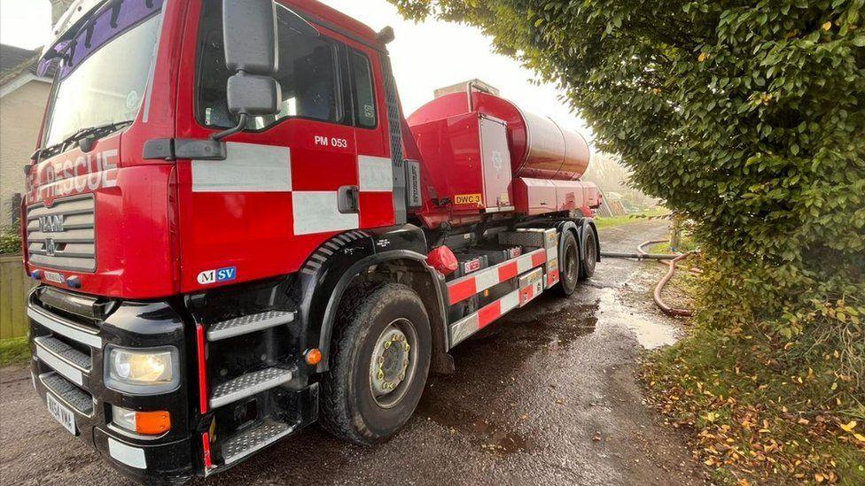 A red truck with silver detail fire service water carrier with fire hoses seen snaking behind