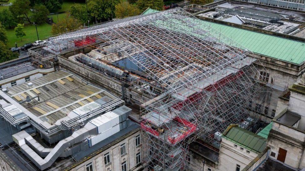 Vast roof of building the middle section has scaffolding across it in a roof shape.