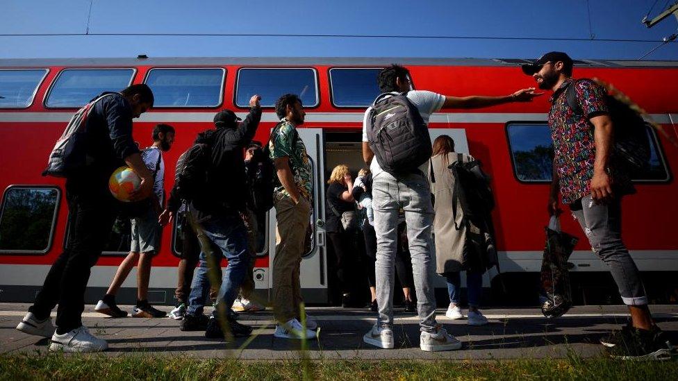 Rail passengers wait outside a regional train to Rostock that stopped due to overcrowding in June