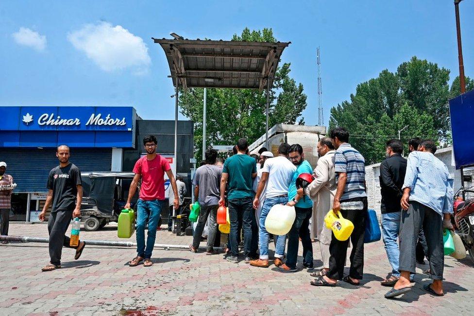 Residents stand in a queue as they hold empty cans to get filled at a petrol station in Srinagar on August 4, 2019