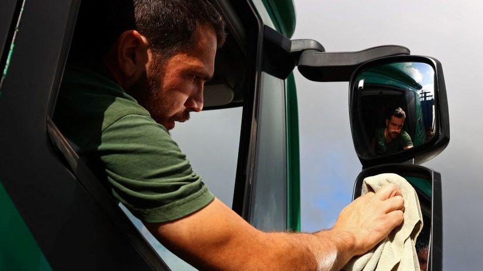 A HGV driver cleang his lorry's wing mirror.