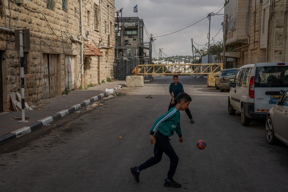 Palestinian boys play football, in front of a checkpoint, just outside H2. Israel restricts movement in and out of the area.