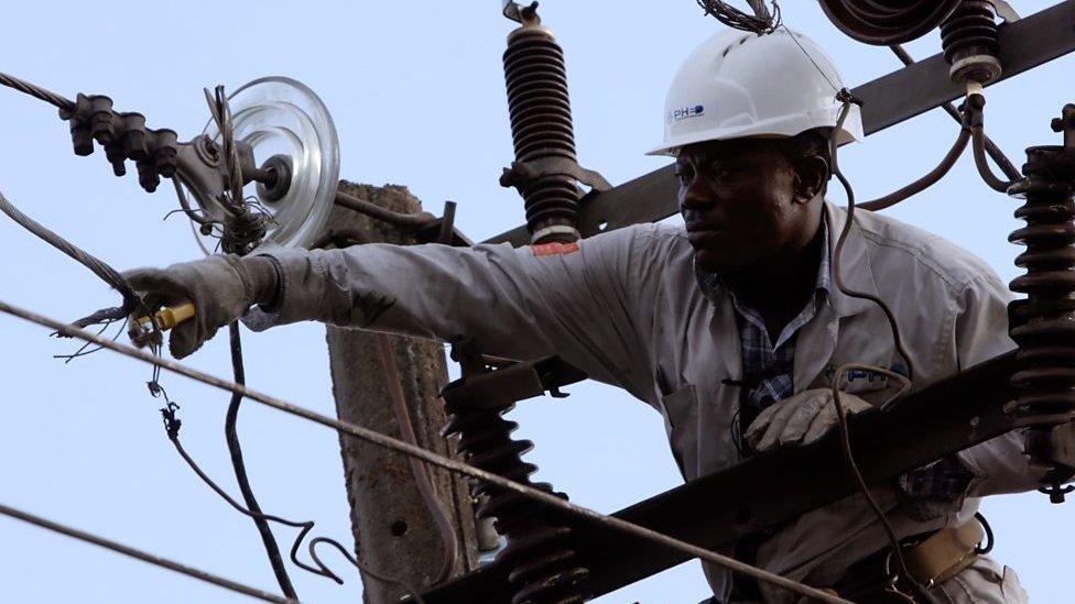 An engineer dressed in protective gear works on an electricity pylon