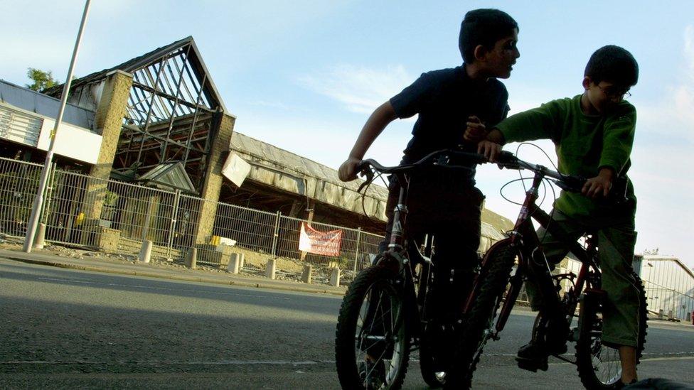 Children play outside an automobile showroom which burnt down in the Manningham district of Bradford July 14, 2001