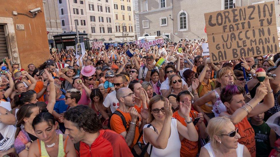 A large crowd has gathered in the streets, waving placards, in this daytime photograph taken within the mass of bodies