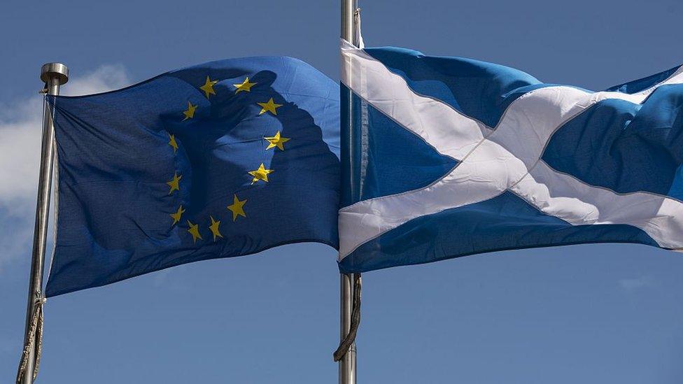 A Scottish Saltire (R) and a European Union (EU) flag fly in front of the Scottish Parliament