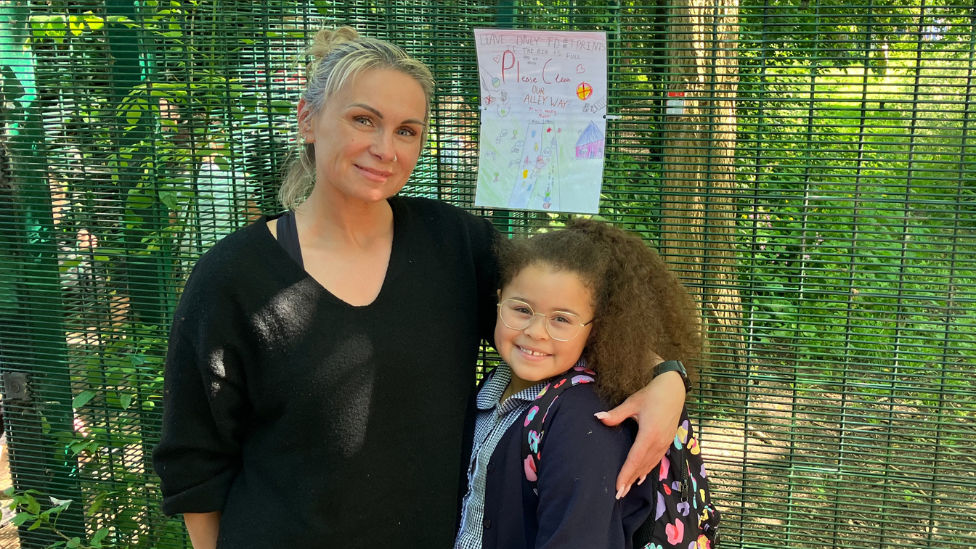 Hazel and her mother standing in front of a fence, arm in arm