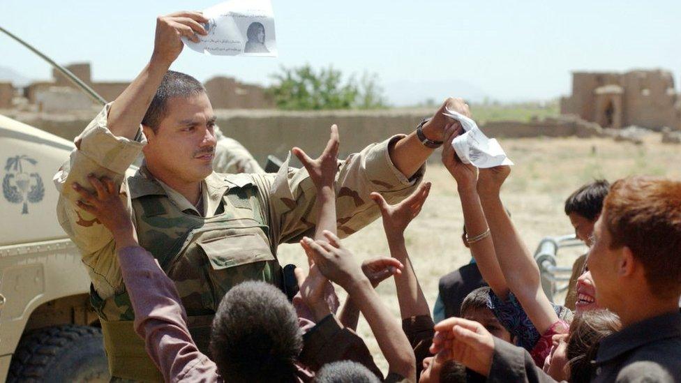 Army Staff Sgt. Rodolfo Arrendondo, from Abilene, TX, hands out flyers from the Army's 345th Psychological Operations Company to a group of local children May 26, 2002 near Bagram airbase in Afghanistan