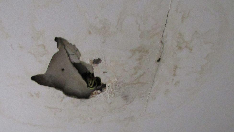 A hole in a white ceiling. There are signs of water damage around it.