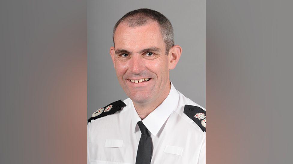 A picture of Hertfordshire Chief Constable Charlie Hall, who has short cropped black hair. He is wearing a white police shirt with a black police tie.