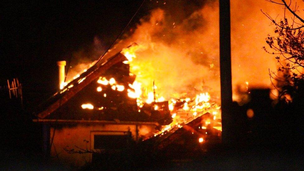 A house well alight in the darkness with flames spread across it