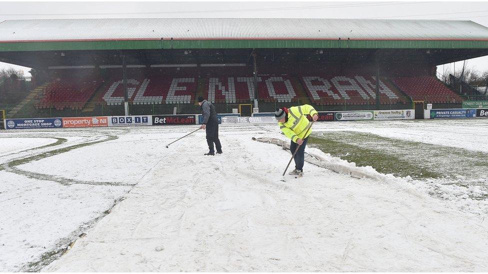 People attempt to clear snow from the Oval football ground