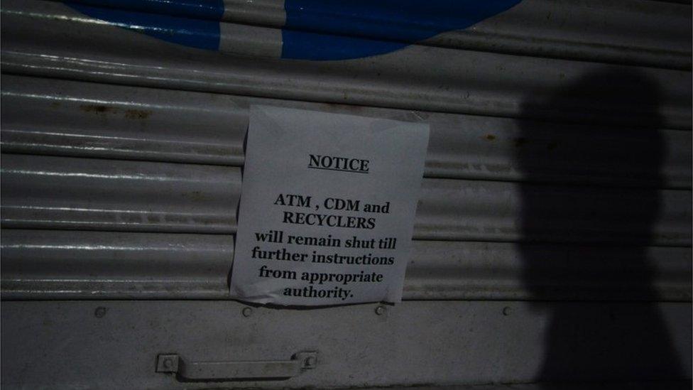 An Indian security guard casts a shadow on a shuttered ATM following the decision to withdraw the current 500 and 1000 INR notes from circulation in Siliguri on November 13, 2016.