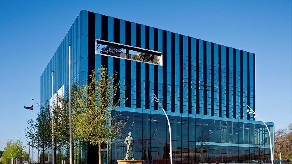 A glass building in a cube design in the middle of a town square.